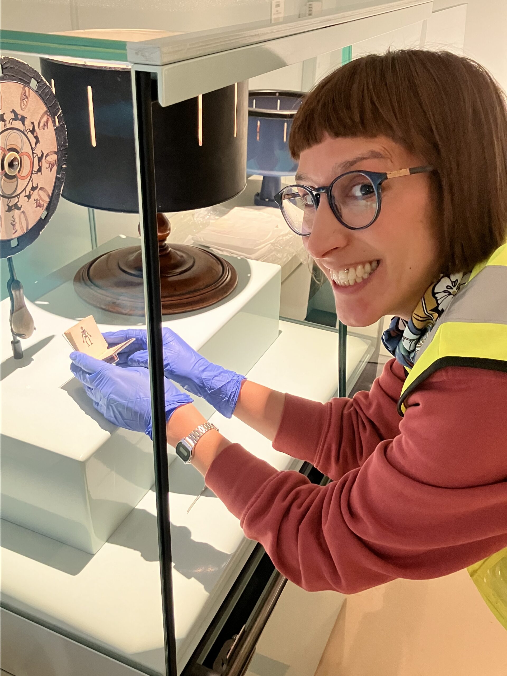 Vanessa grins as she places an object in a glass display case.