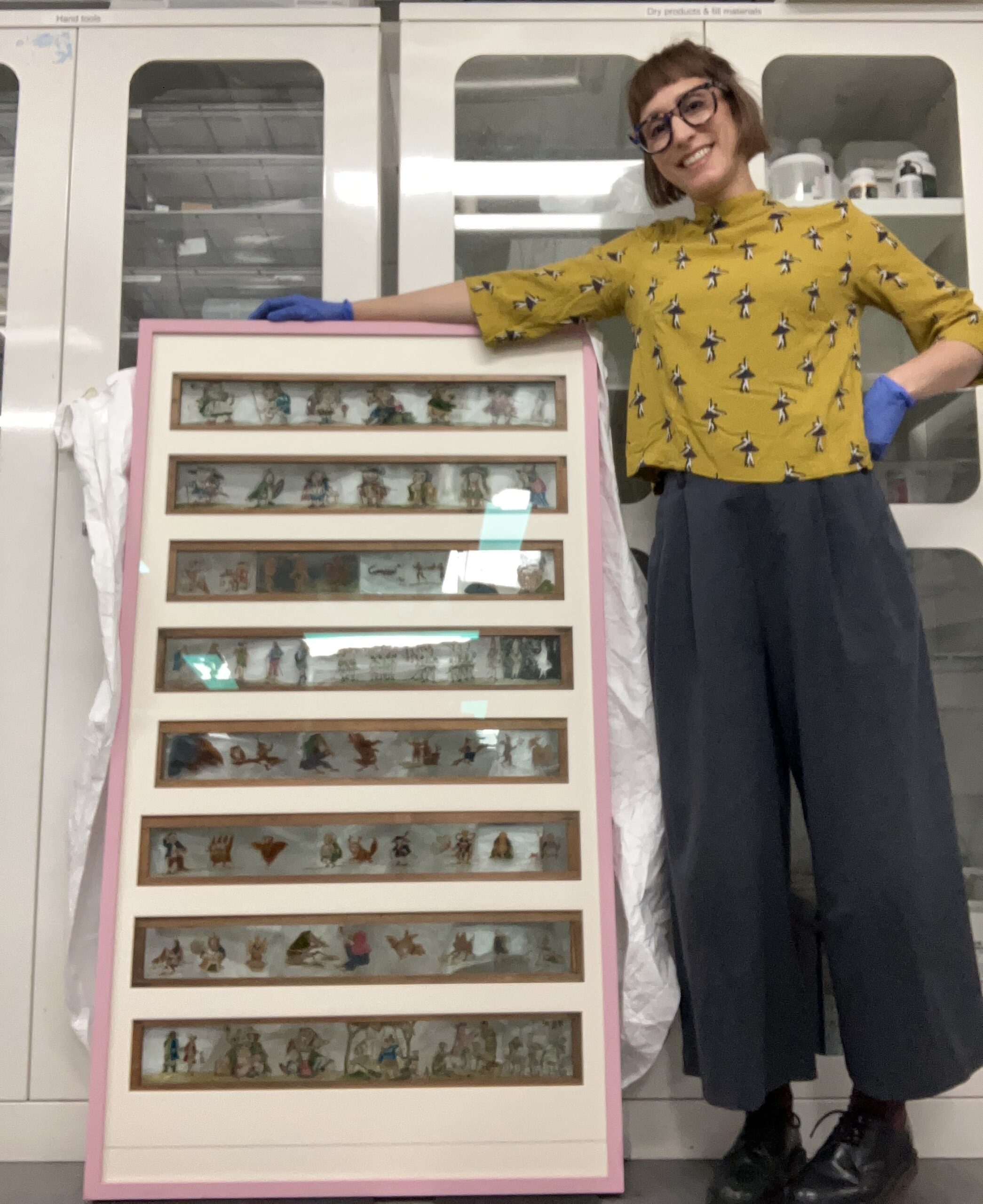 Vanessa smiles as she stands next to a large cframe displaying magic lantern slides