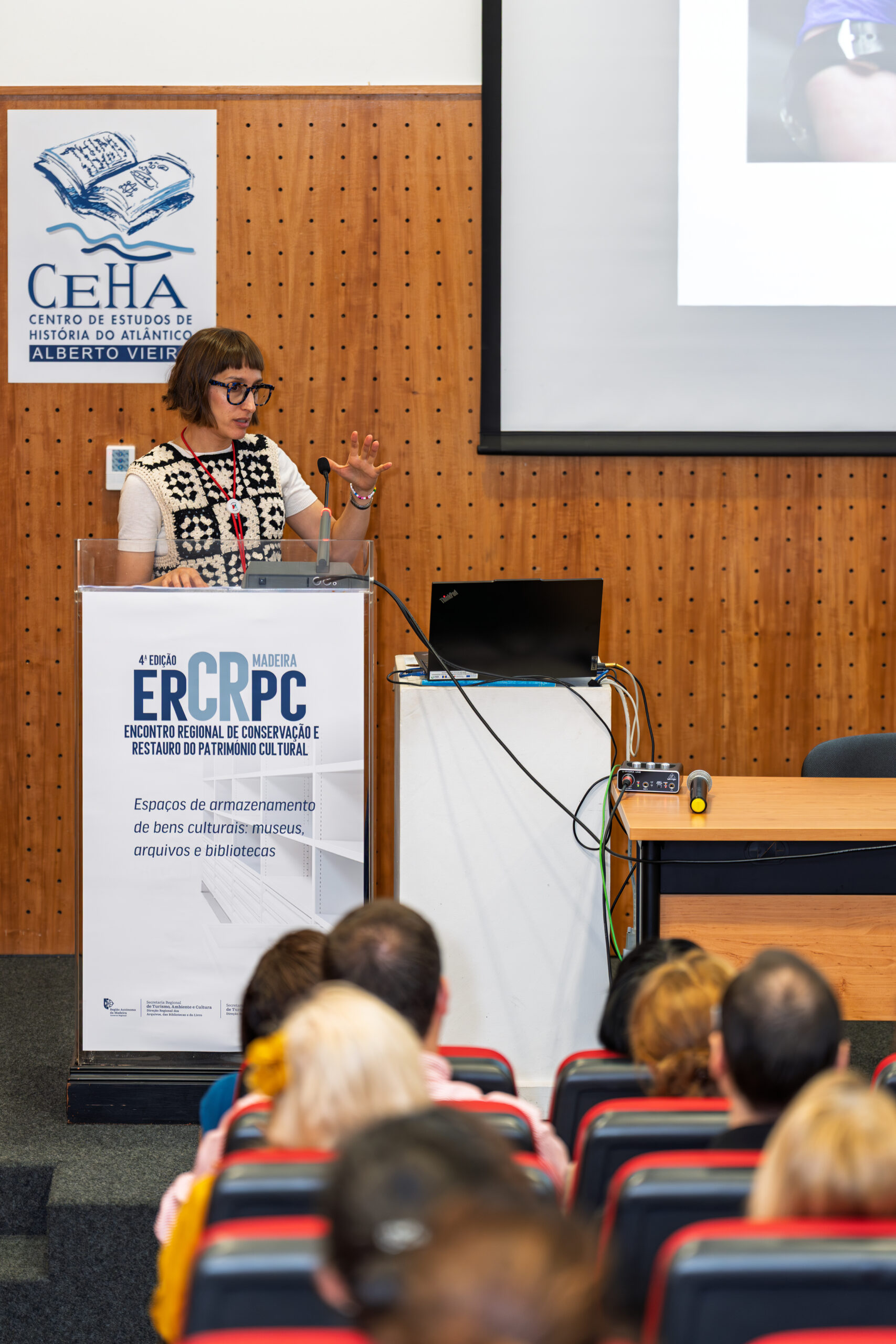 Vanessa speaking from a lectern at a conference. She's wearing a crochet top and glasses.