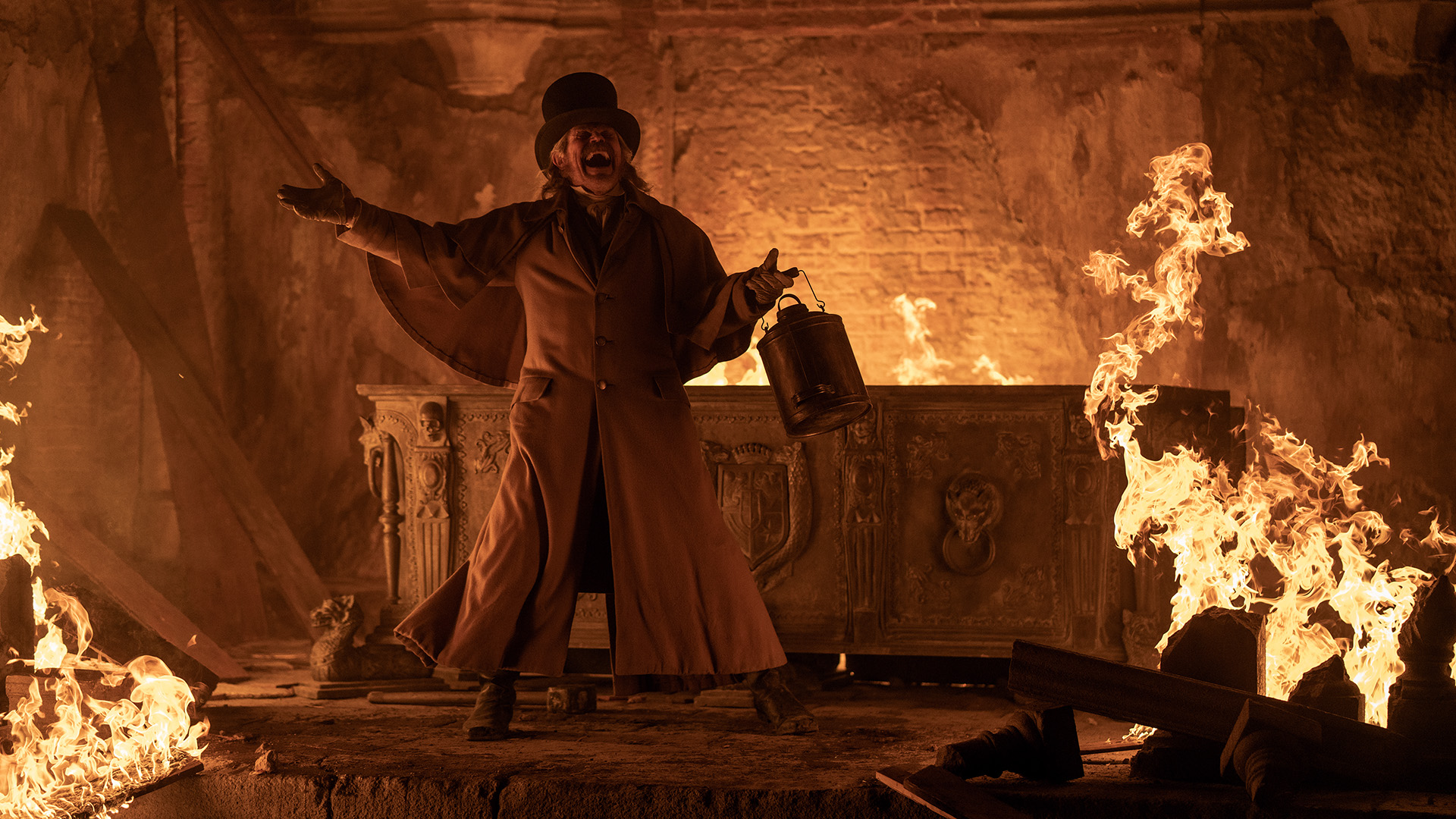 A man in 19th-century greatcoat and top hat stands in a crypt. He swings a tin can in one hand and exclaims as flames lick at a sarcophagus behind him.