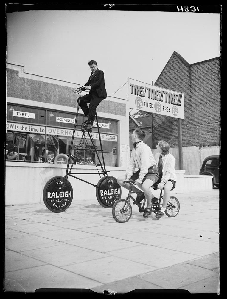 Couple cycling together alongside a man riding a very tall bike