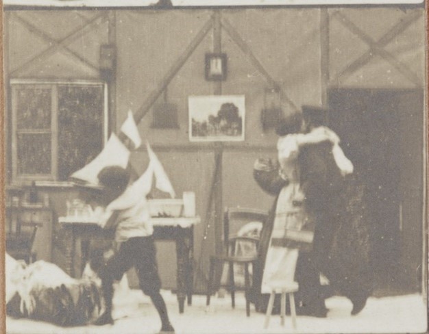 Frame from a film showing a woman embracing a man and a child playing