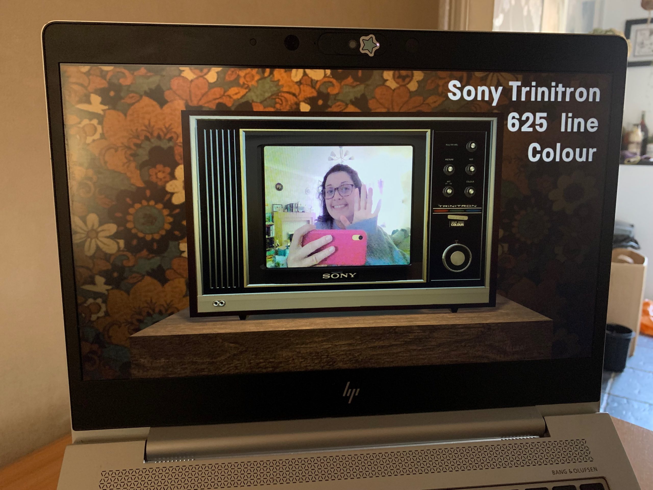 Laptop screen showing computer model of old TV screen displaying a webcam feed of a woman waving