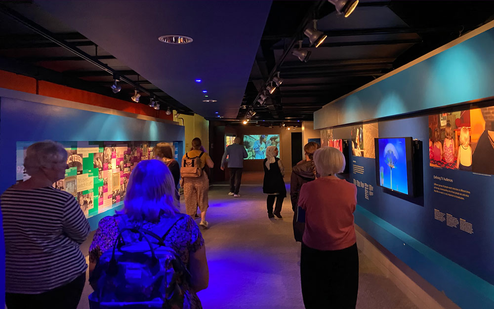 A group of people walk through a dimly-lit museum gallery