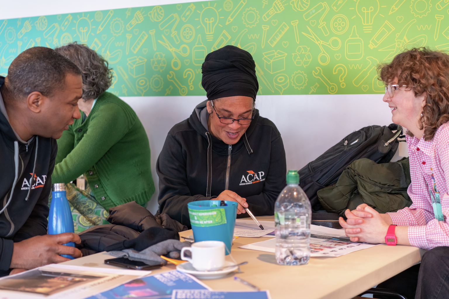 Three people sit at a table looking at different designs on paper