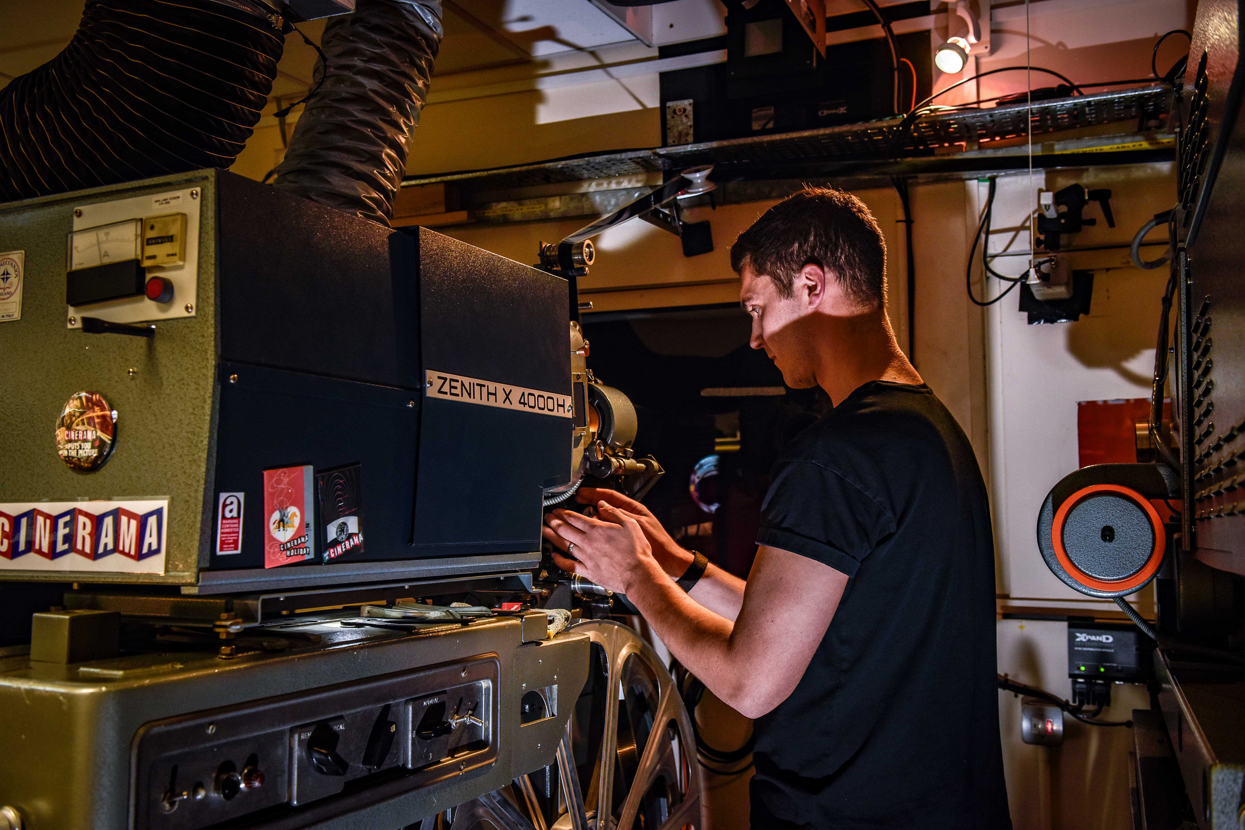 A man adjusts a film projector inside a projection box