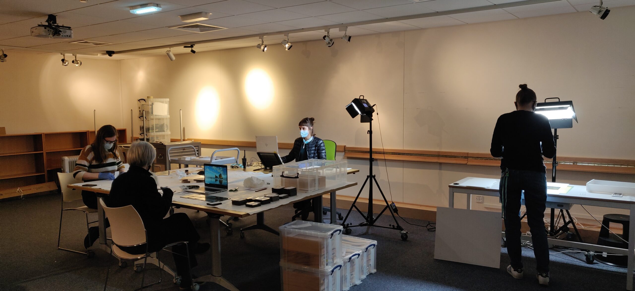 museum staff wearing face coverings work on magic lantern slides in a room lit with task lamps