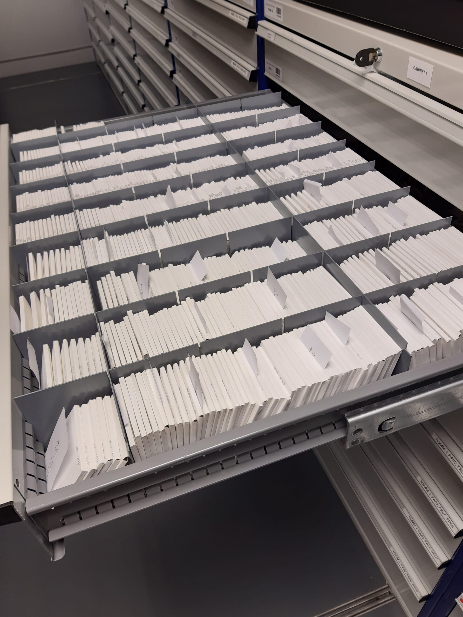 A plan chest drawer filled neatly with white envelopes containing magic lantern slides