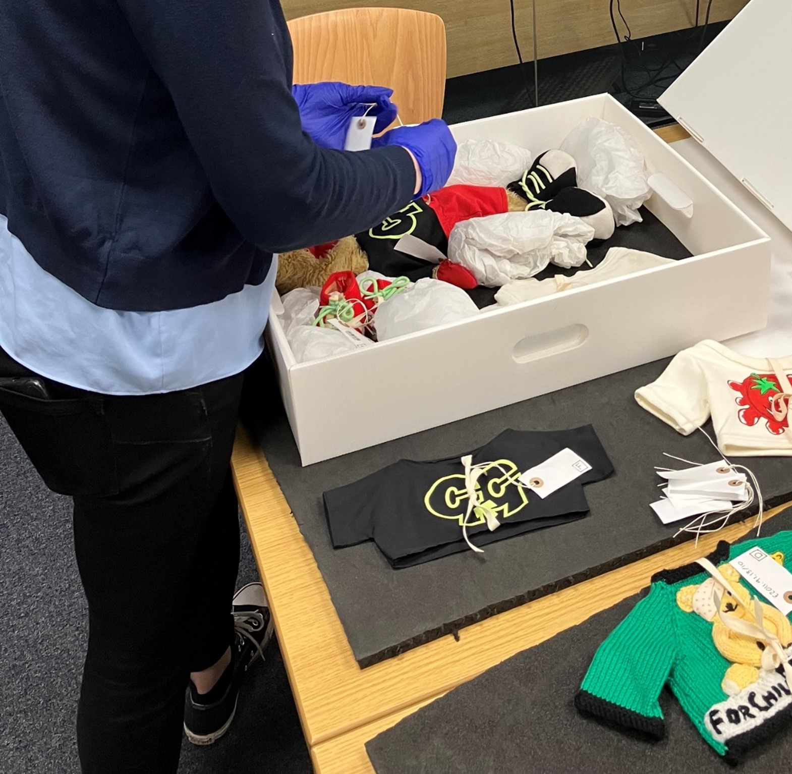 The legs and torso of a person standing to pack items belonging to a TV puppet into an archival box