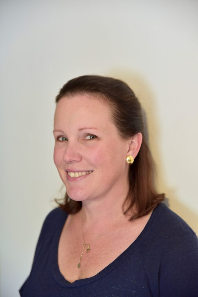 Lucy is a white woman with shoulder-length hair, wearing a navy top