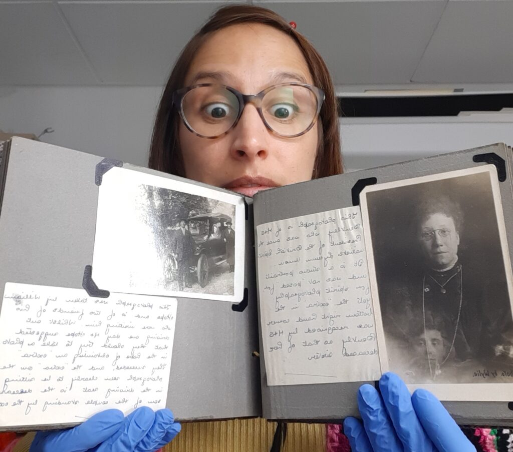 Vanessa, a white woman with brown hair and glasses and wearing blue nitrile gloves, holds up an open photo album
