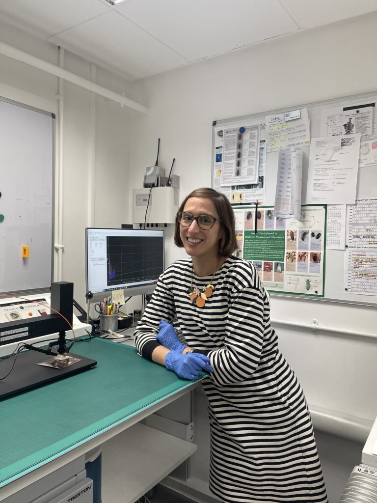 Vanessa, a white woman with short hair and glasses, leans on a bench with conservation equipment