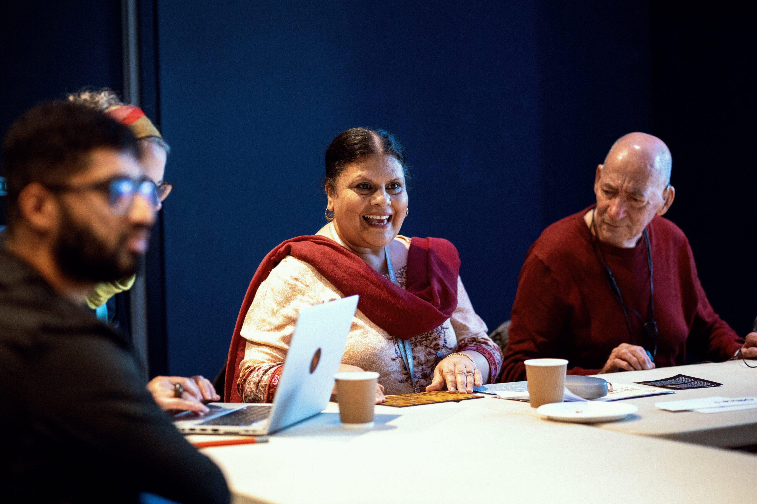Four people sit around a table; the woman in the centre feels a sample of material