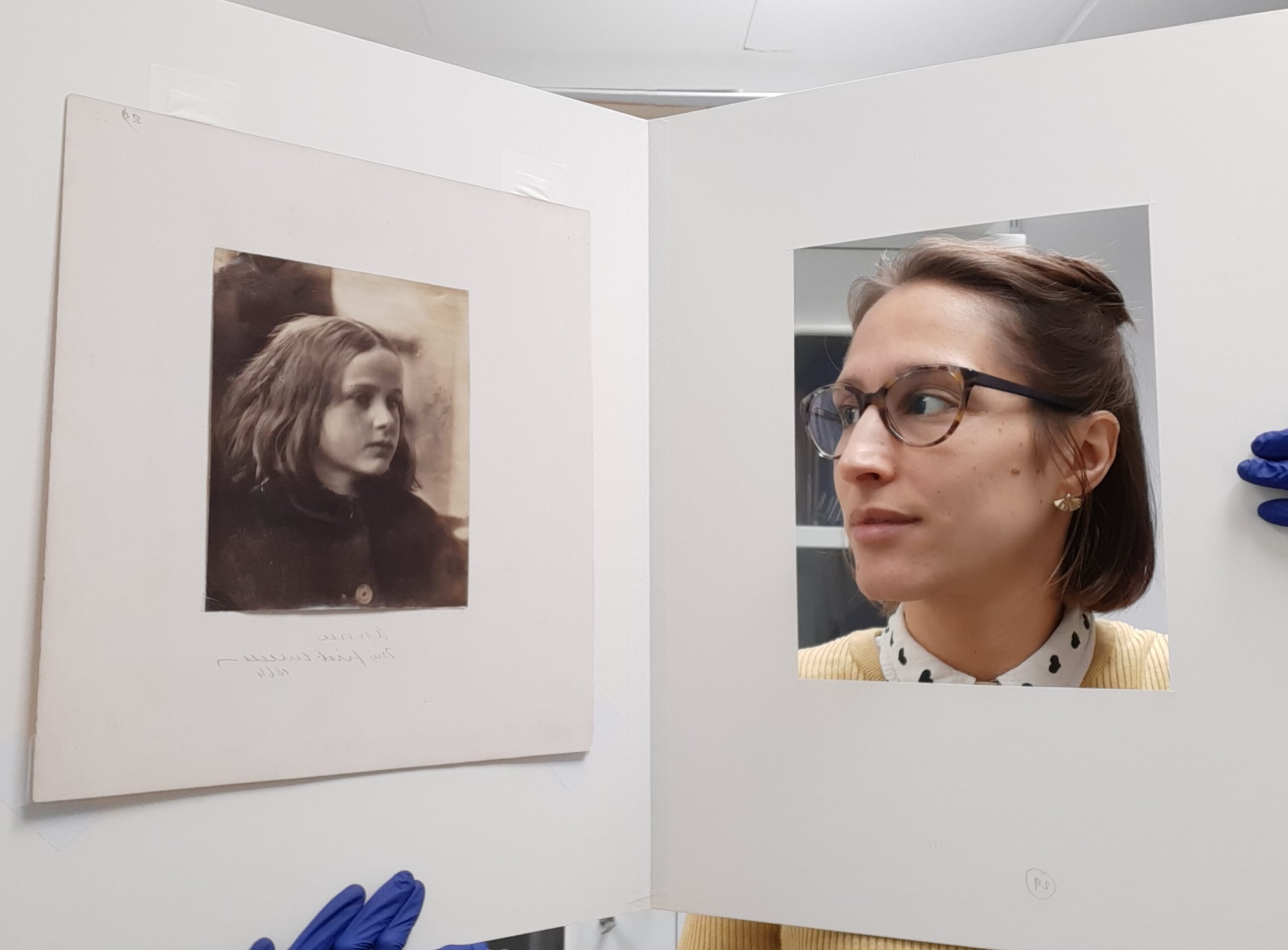 Vanessa looks through a window in a card sleeve at a portrait of a young girl