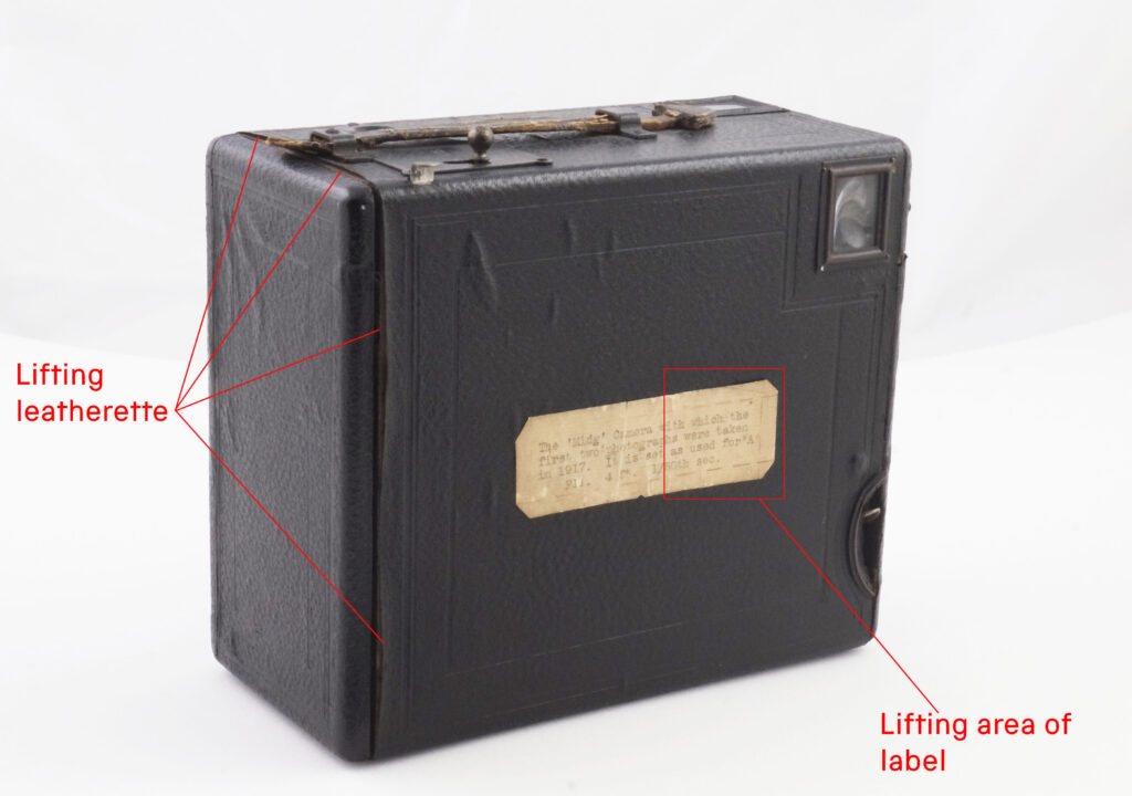 A box camera with red annotation showing where the covering material and label are peeling away