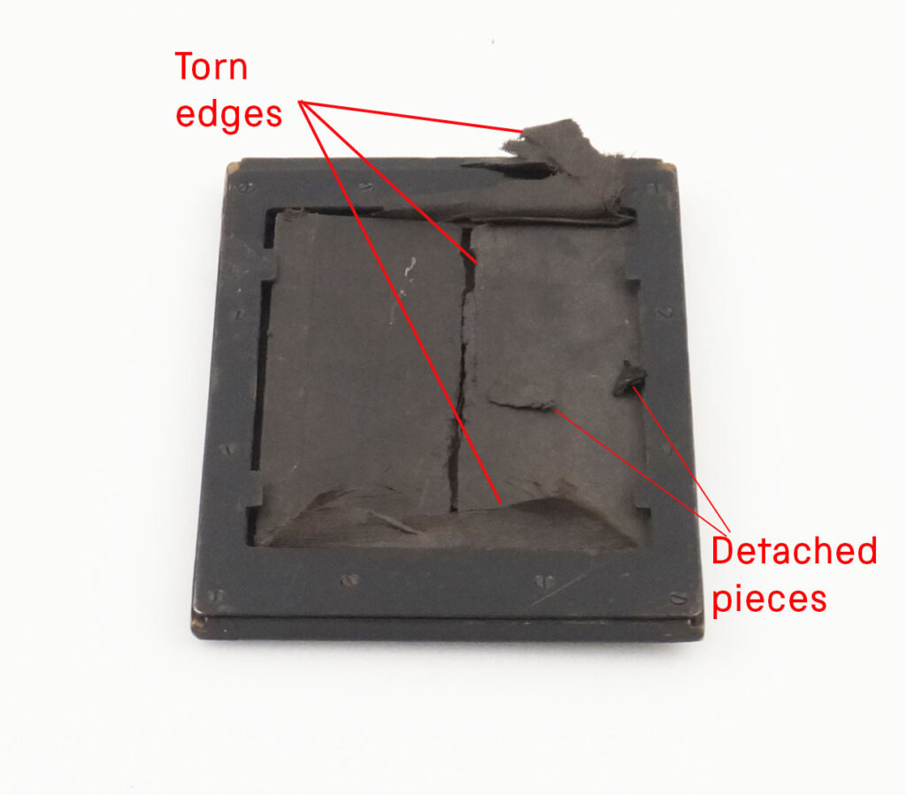 Square hood of a box camera with red annotation showing where parts of the material have come away