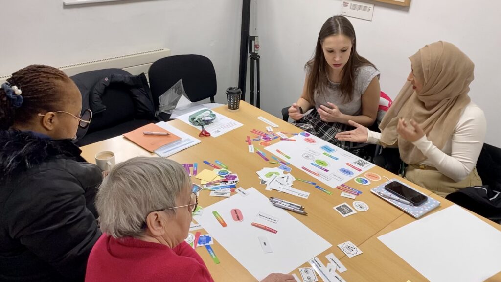 Four people in conversation around a table spread with colourful paper labels.