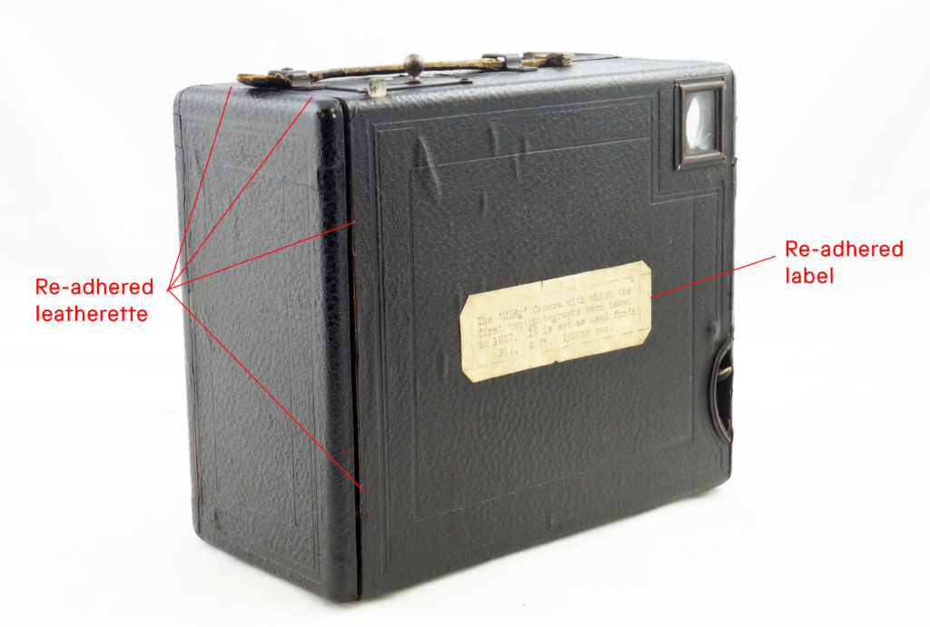 A box camera with red annotation showing where the covering material and label have been reattached