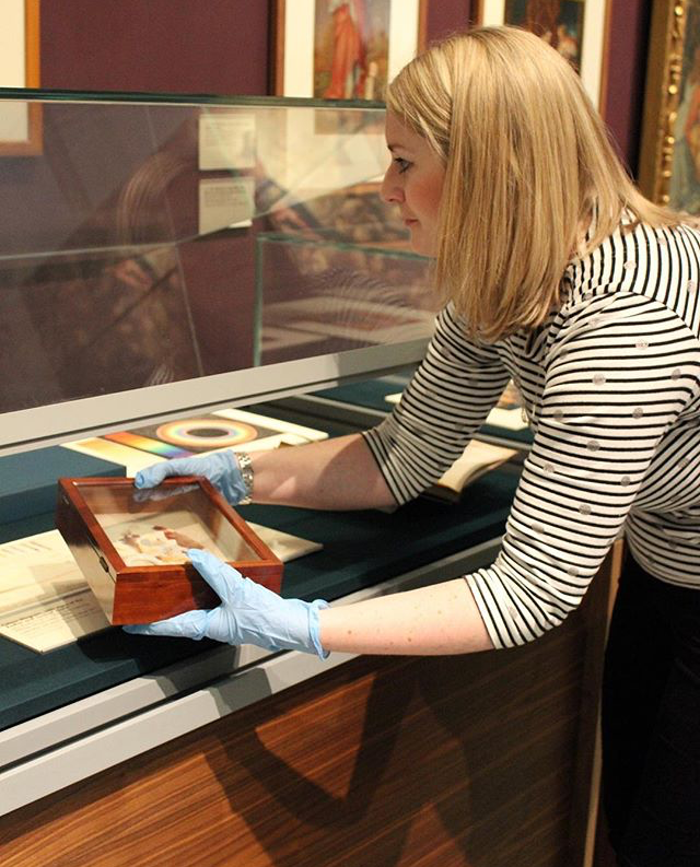 Hannah carefully lifts an object into a glass display case
