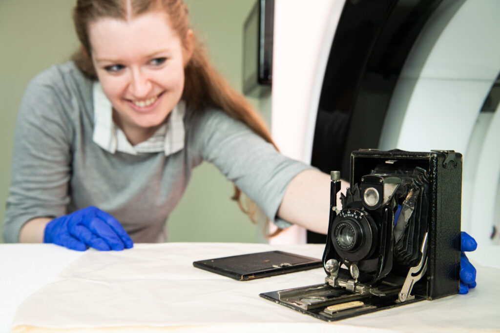 Conservator Eleanor Durrant placing a black box camera on the white bed of a large scanner