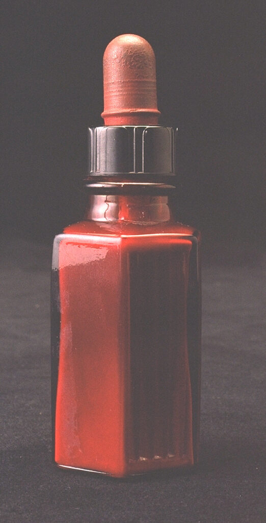 Glass bottle with a pipette, filled with red liquid