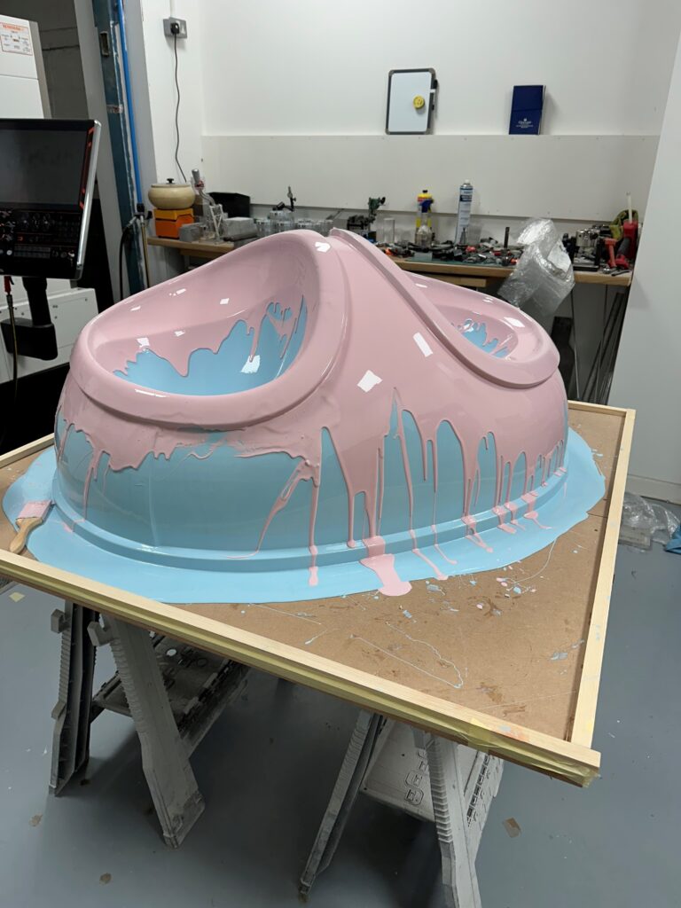 The hip part of the techno trousers mid-painting, with light pink and blue paint dripping onto the workbench