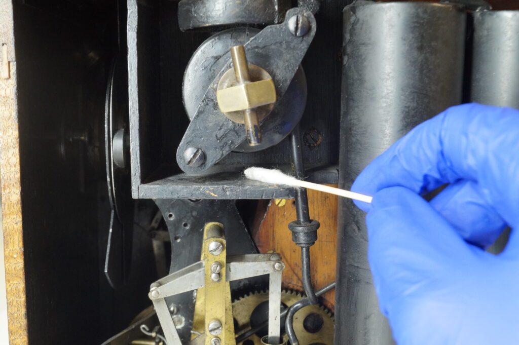 A hand in a blue nitrile glove swabs the camera mechanism with a cotton bud