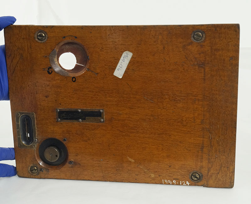 Hands in blue nitrile gloves holding the door of a wooden box camera