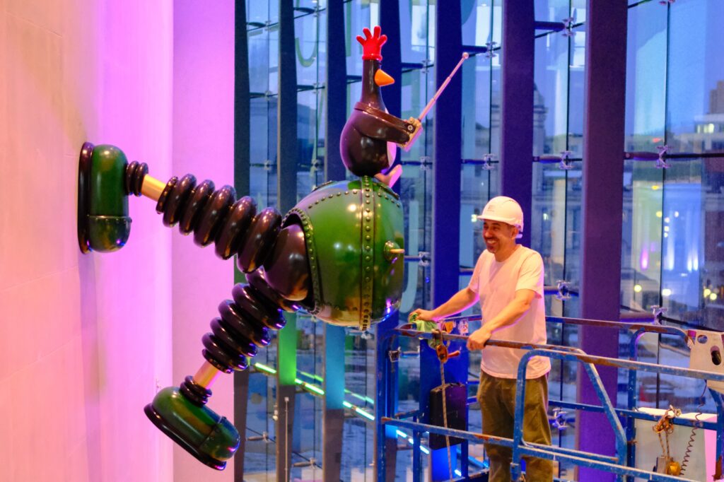 Andy stands on a cherry picker smiling at the finished techno trousers installation