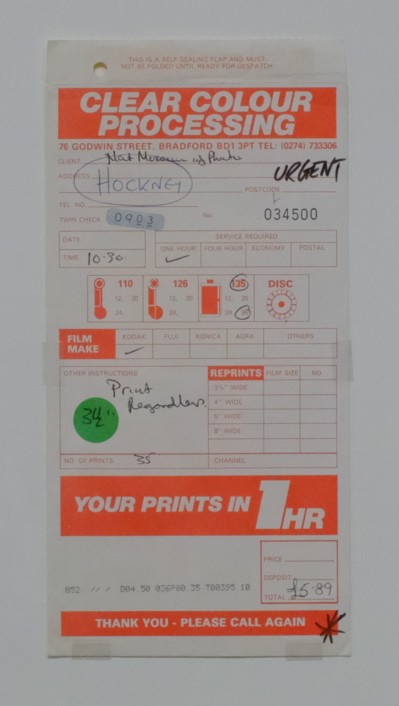 White and orange paper envelope from a photo shop. Hockney's note reads 'print regardless'.