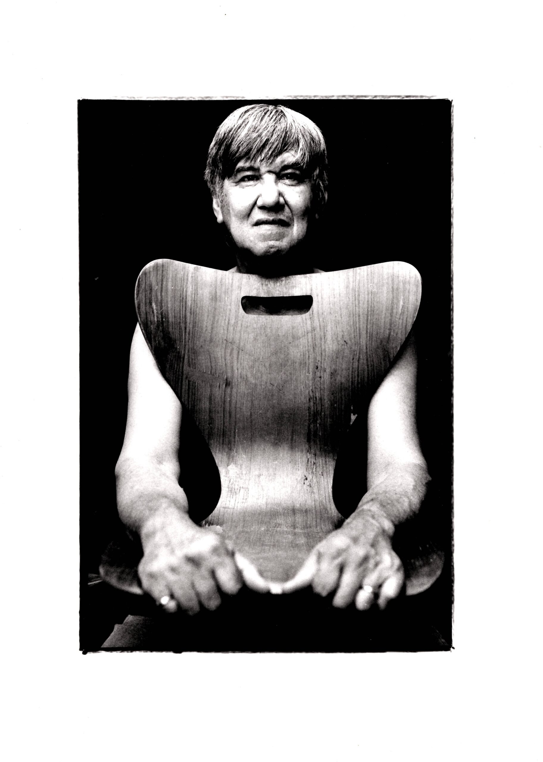 Black and white photo of Morley sitting with a chair on his knees, the back covering his torso