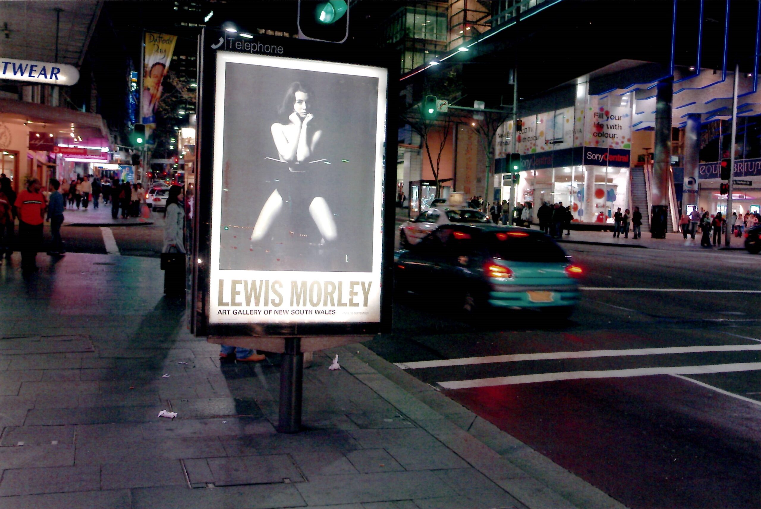 A billboard on a busy nighttime street with a poster of Morley's work