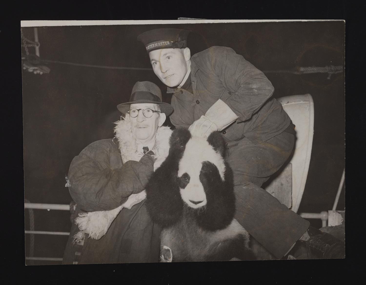 A suited man and a man in ship's quartermaster's uniform pose with a baby panda