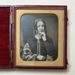 A photographic portrait of a woman with ringlets, resting her chin in her hand. The picture is in a case lined with red velvet.