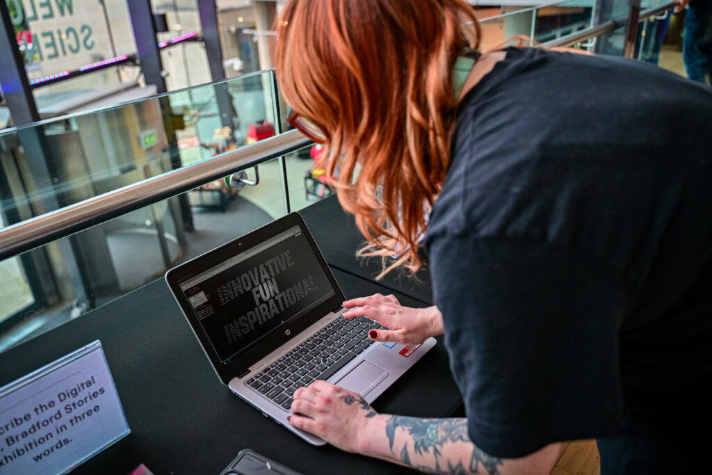 A person with red hair and forearm tattoos creates word art on a laptop