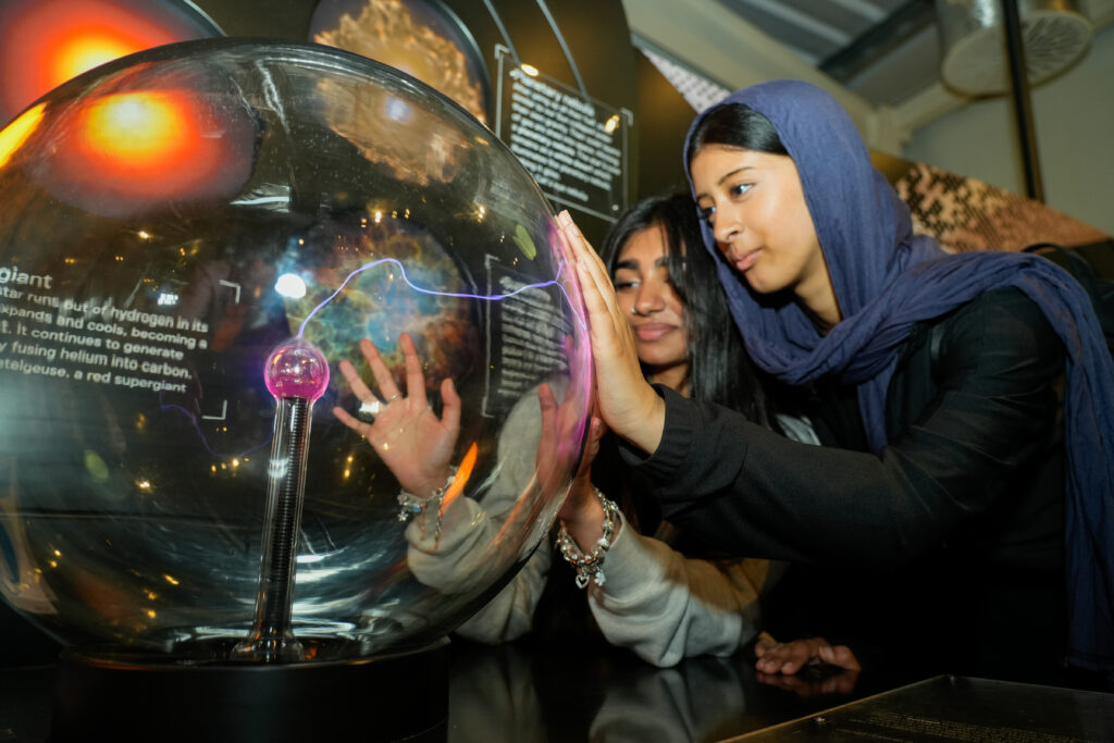 Two South Asian girls put their hands on a glass sphere in a science exhibition