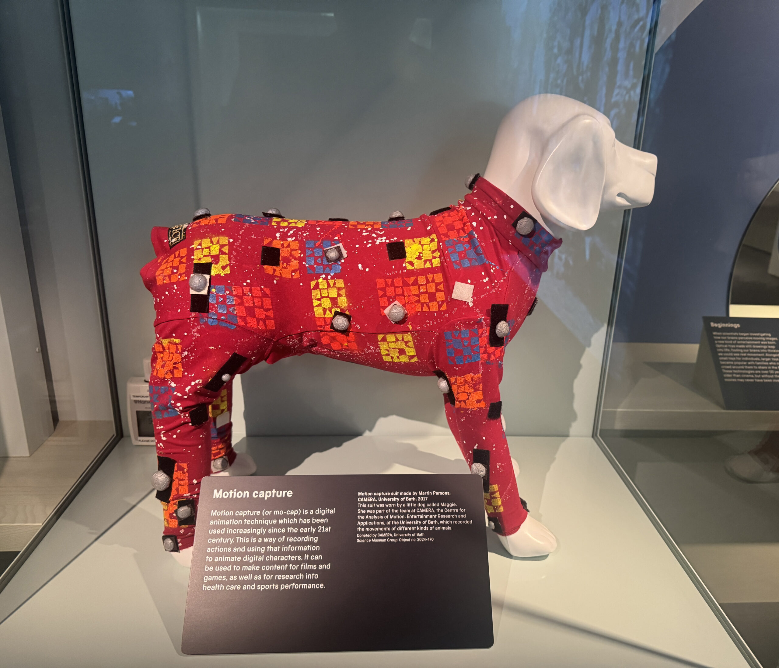 A bright red motion capture suit for a dog, with orange, yellow and blue patterns. The suit is on a white plastic model of a dog.