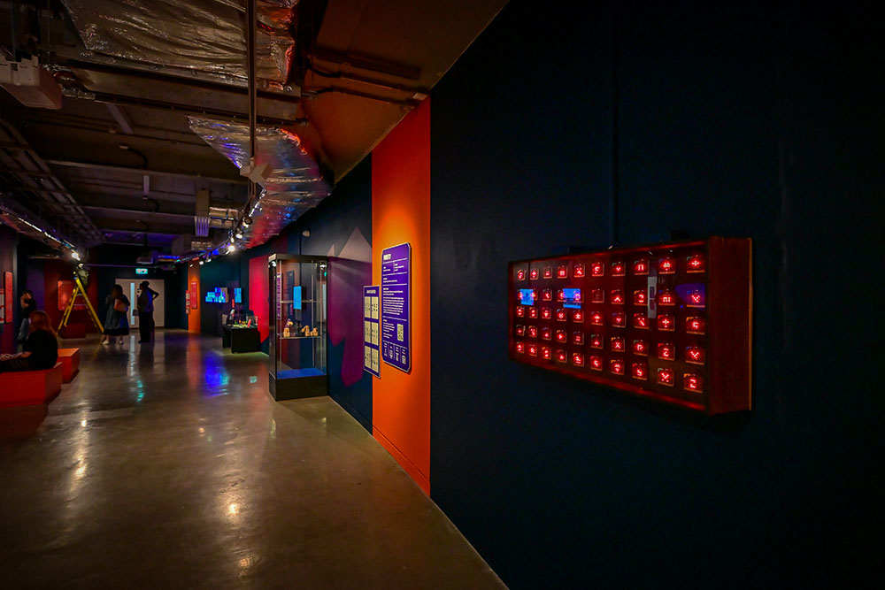 A rectangular artwork made up of red microbits on a dark gallery wall
