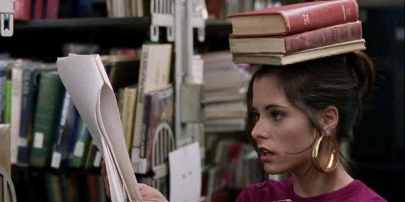 Mary (Parker Posey) balancing a stack of books on her head in a library