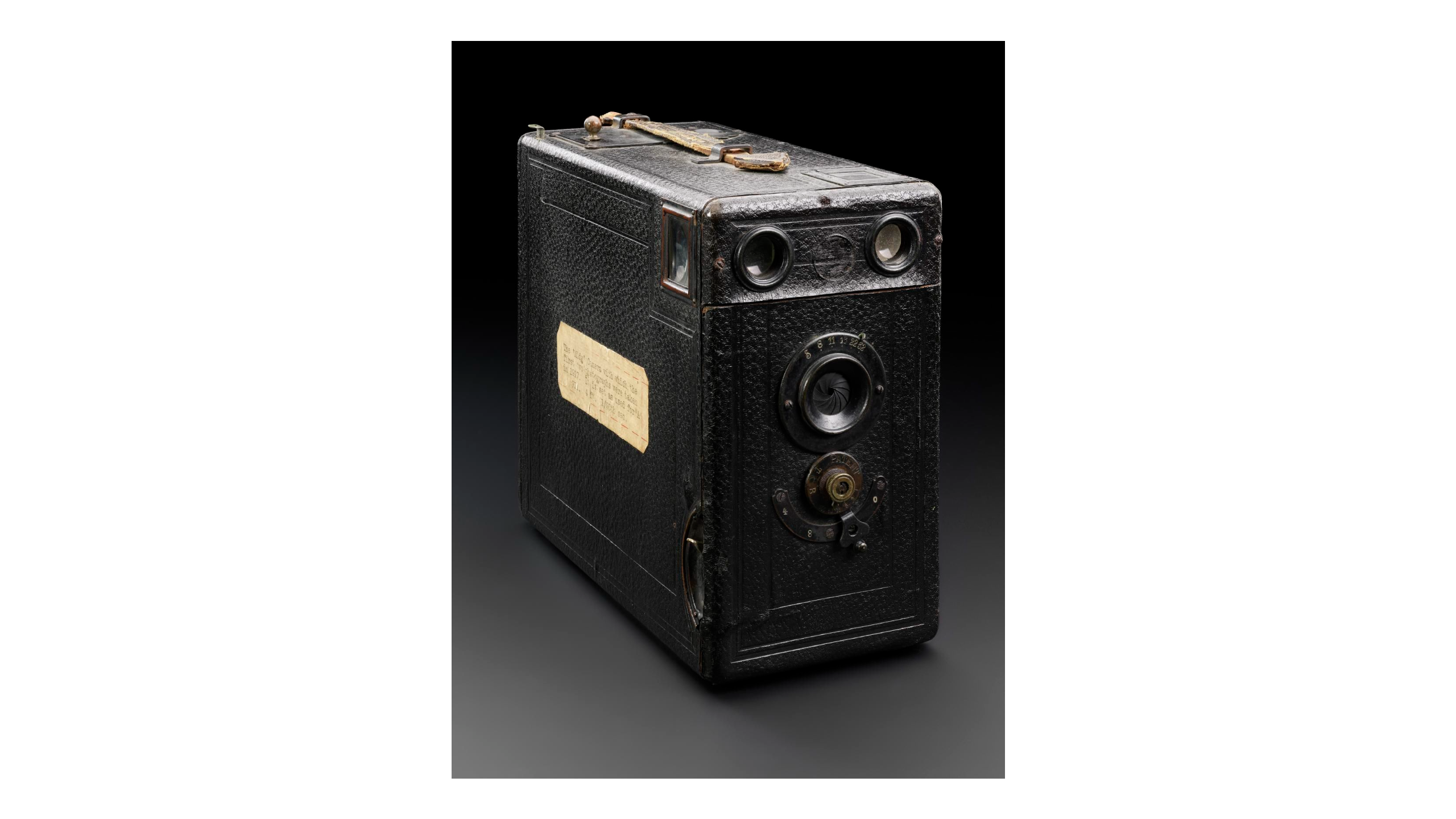 A blakc box camera with a paper label on one side, against a dark gray background