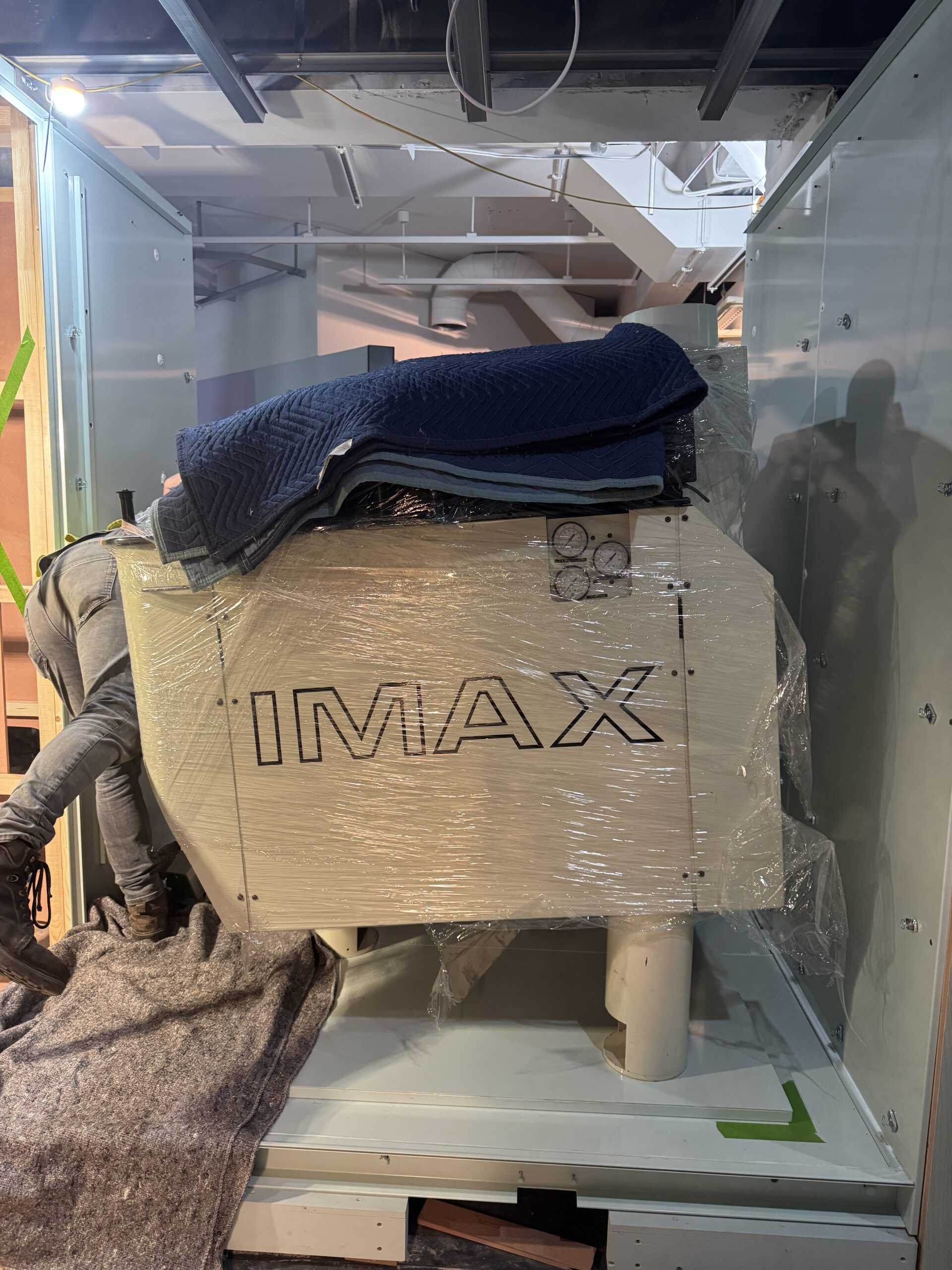 Large boxy IMAX projector covered in plastic wrap and blankets being unwrapped on gallery