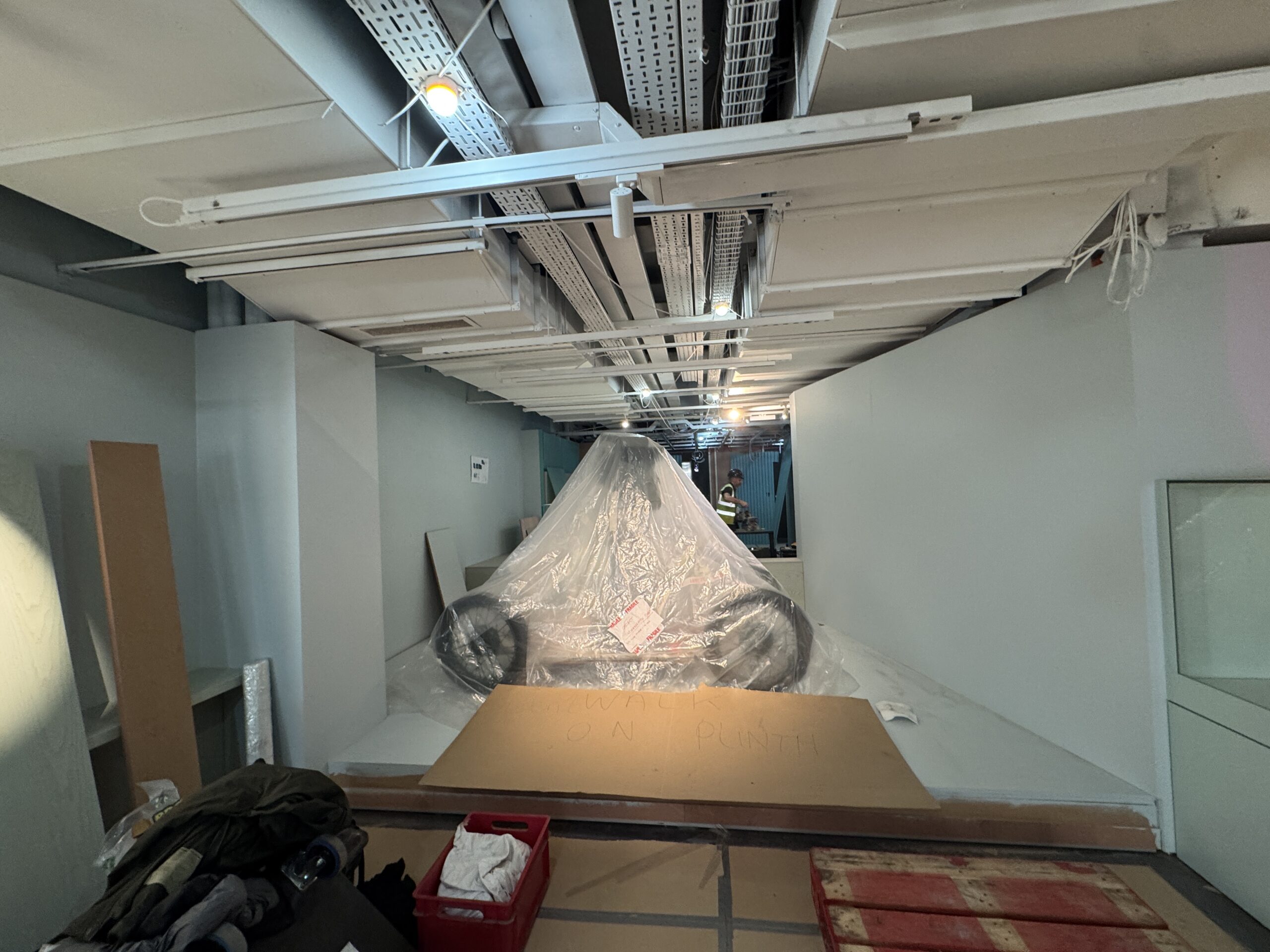 A large camera on a dolly, under plastic sheeting in the gallery mid-install