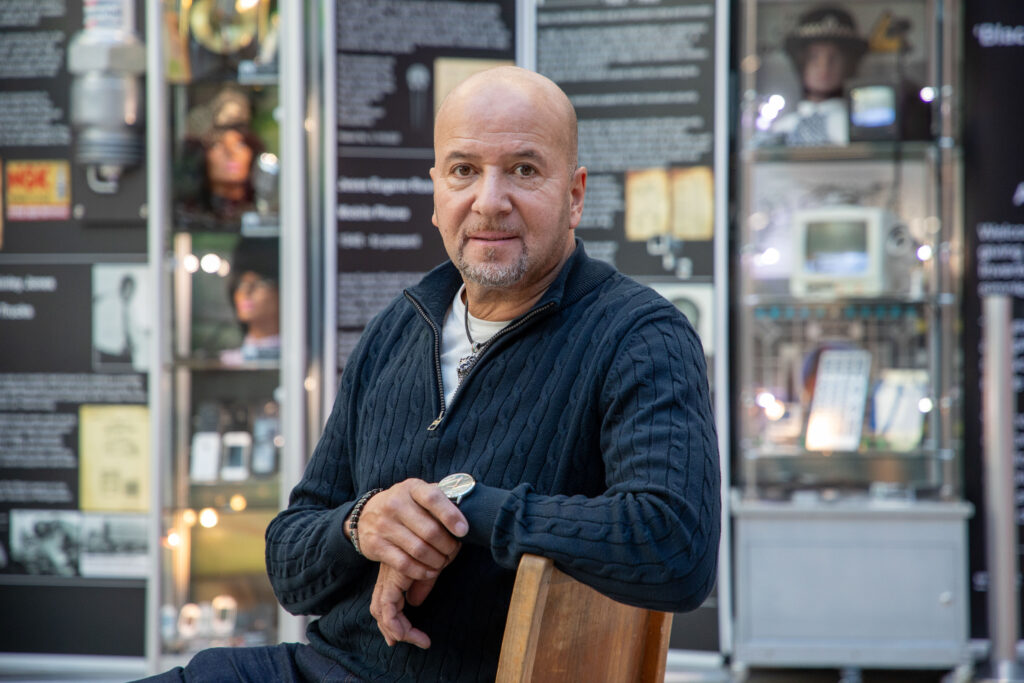 Chris sits in front of his exhibition with his arm on the back of the chair