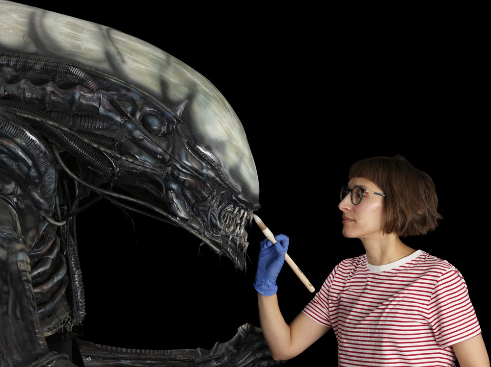 Vanessa using a brush to conserve the 'Alien' replica, which is larger than her.