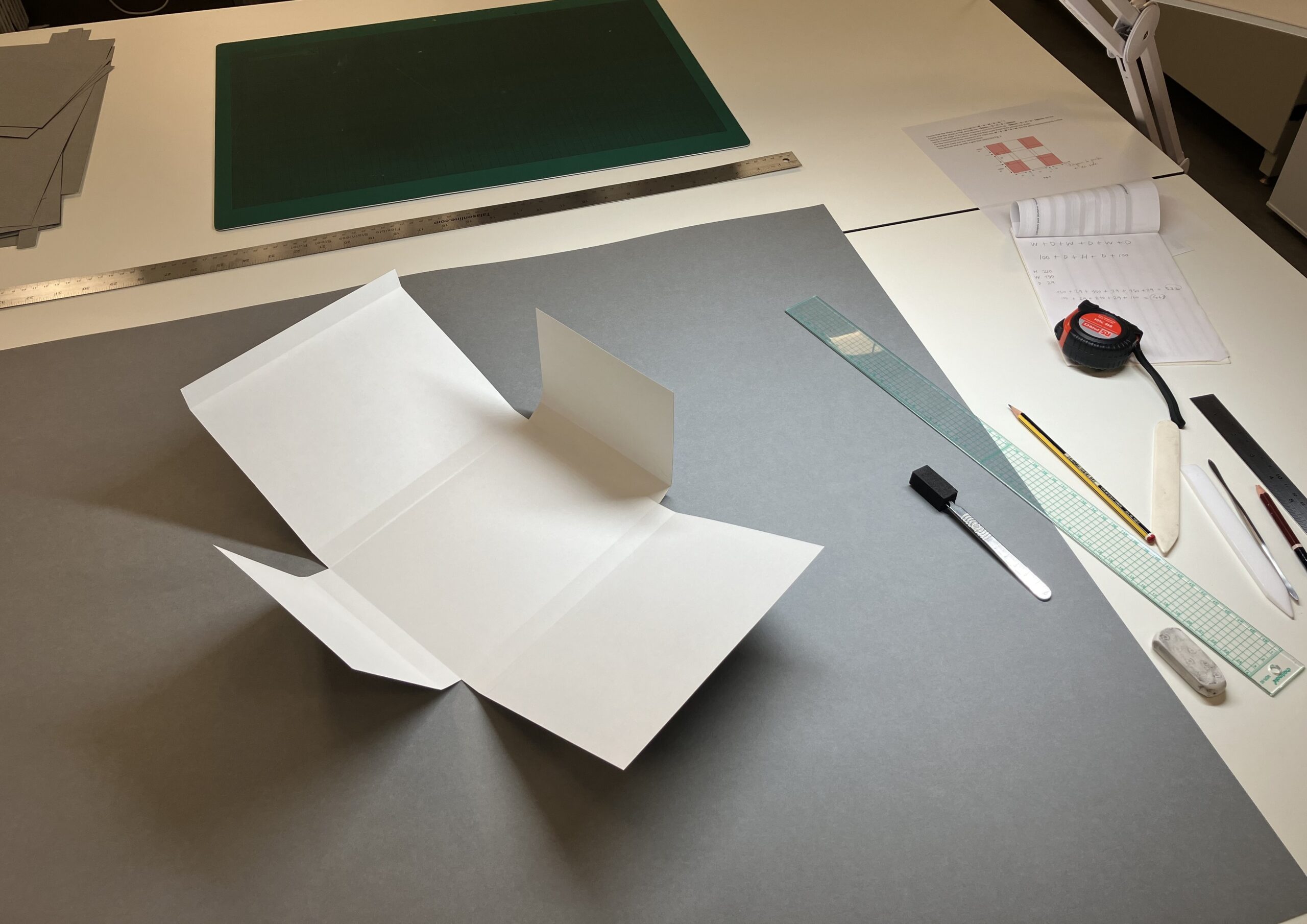 A folder template laid on top of grey card on the workbench, with various tools to the side.