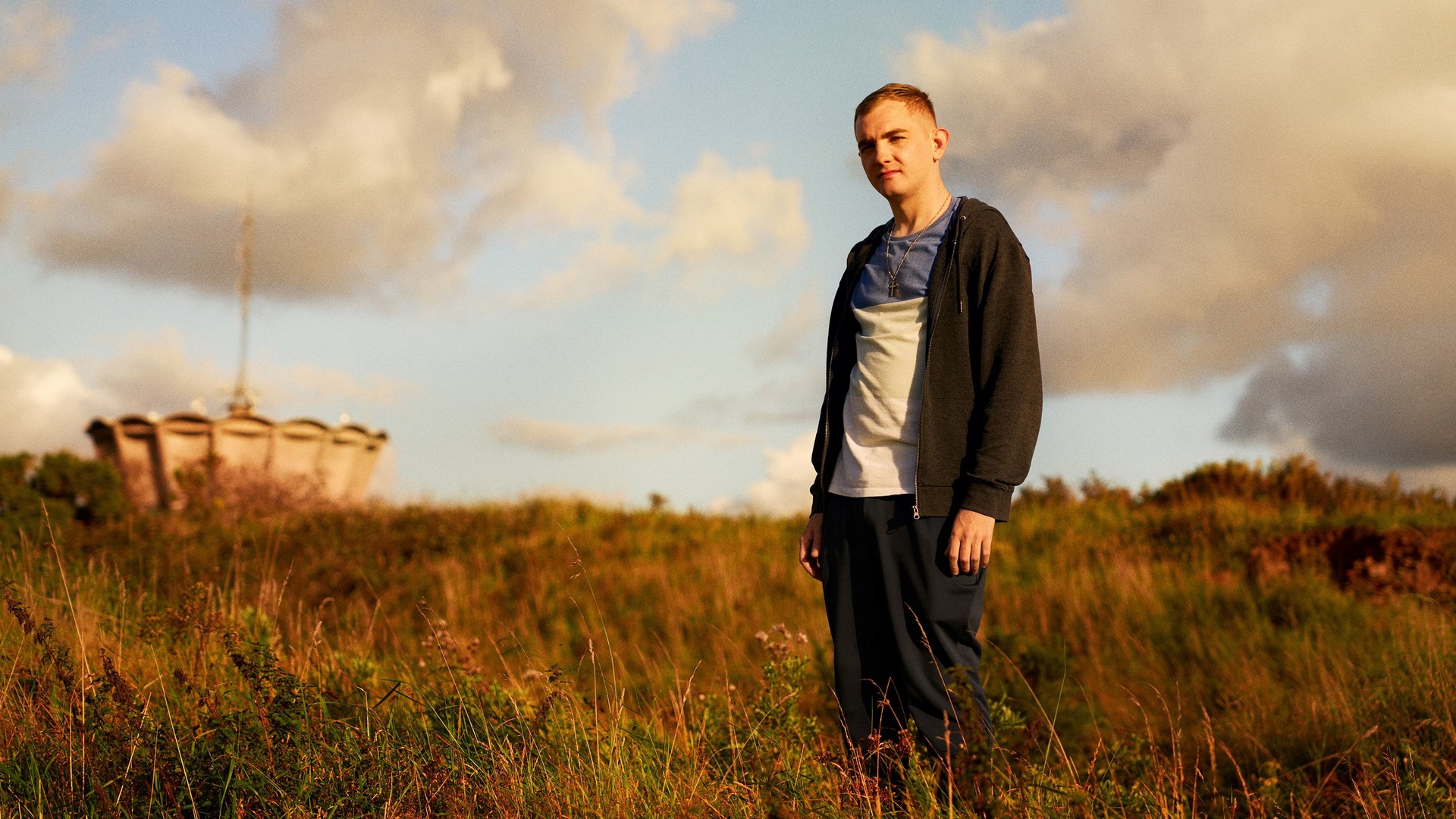 A young man stands in an overgrown field in golden hour sunlight