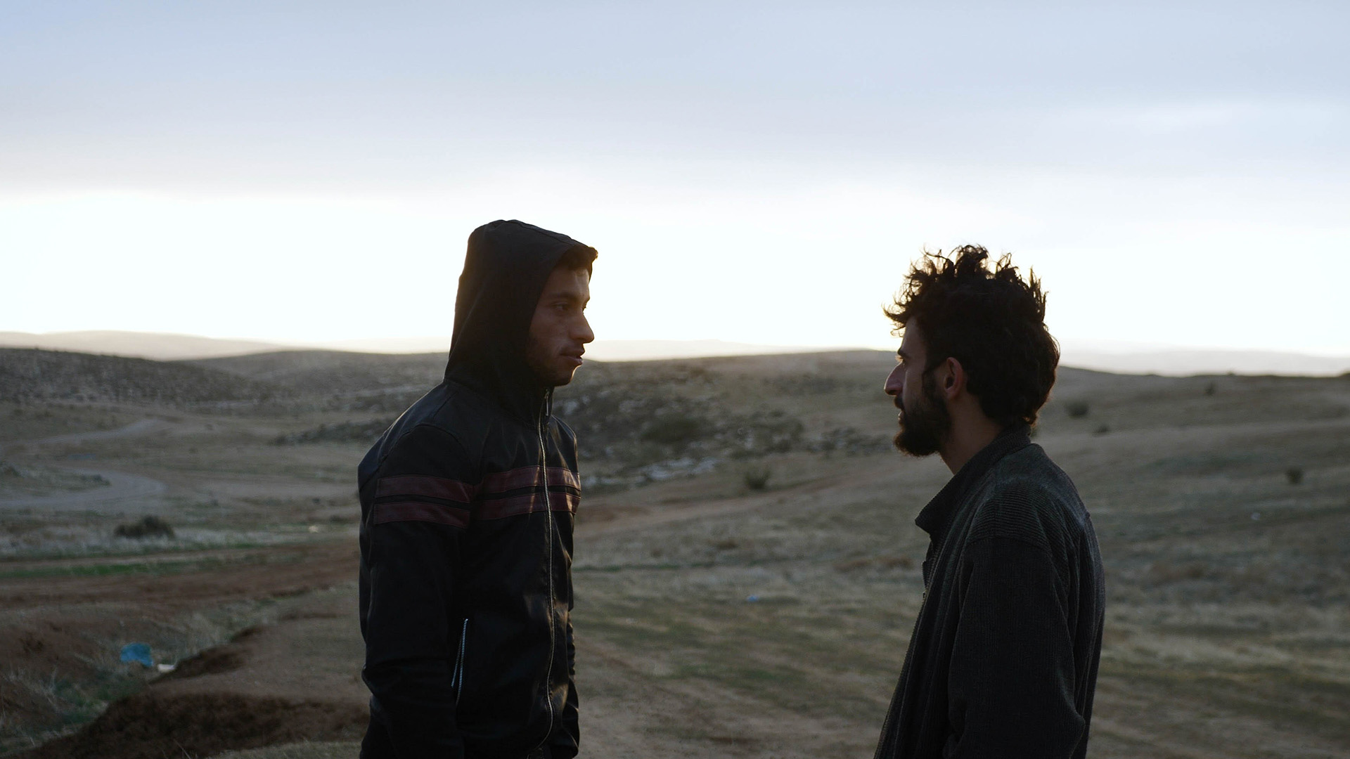 Two men face each other atop a hill in a Palestinian desert landscape.