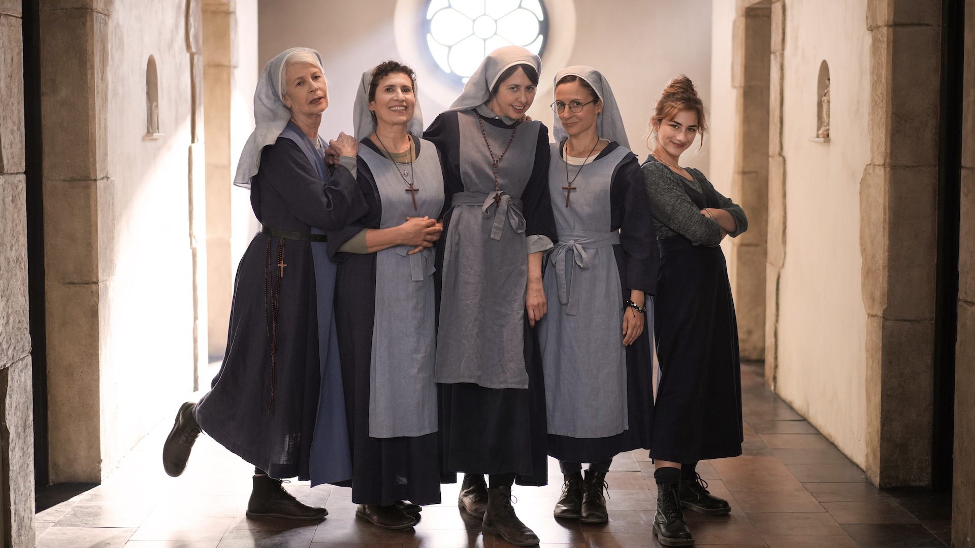 A group of four nuns in habit and a woman in regular dress stand in a group, smiling mischievously.