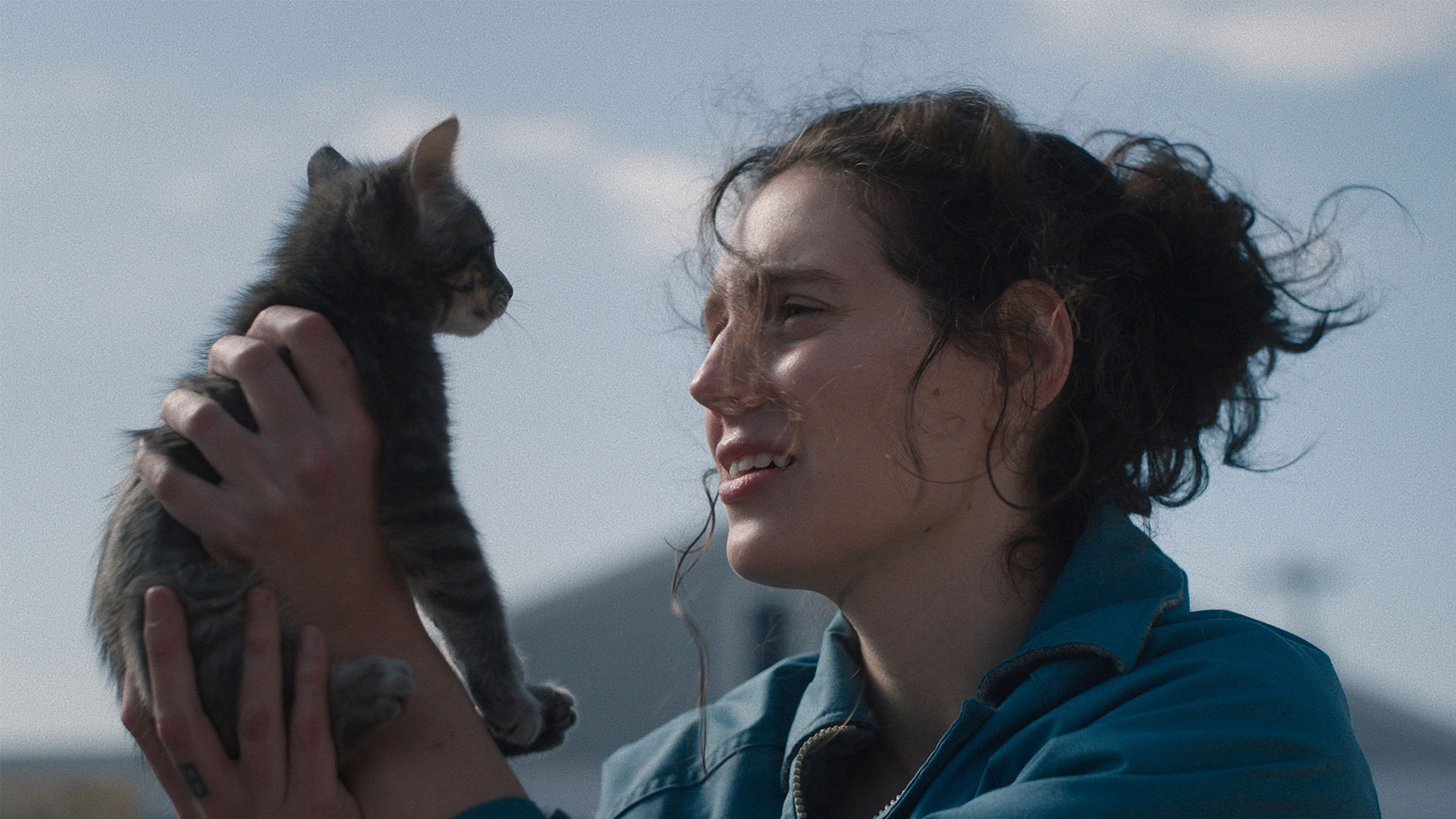 A woman with curly hair holds up a small kitten