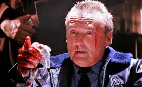 Dennis Hopper holds up a bloody hand and bleeds from his nose and temple.